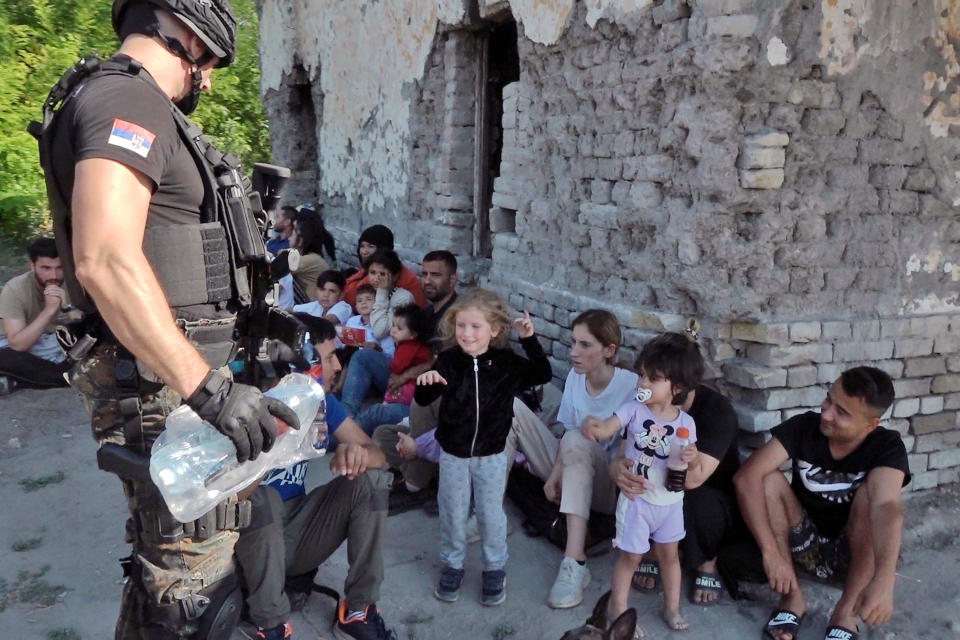 In this photo provided by the Serbian Interior Ministry, Serbian Police officer gives water to migrants near village of Horgos, Serbia, Tuesday, July 26, 2022. Serbia's police broke up a people-smuggling gang near the border with Hungary early on Tuesday, and found various weapons and hundreds of passports and other documents taken from migrants trying to reach Western Europe, officials said. Police also discovered 120 migrants, including women and children, during the operation in the area of Mali Horgos, a statement said. (Serbian Ministry of Interior via AP)