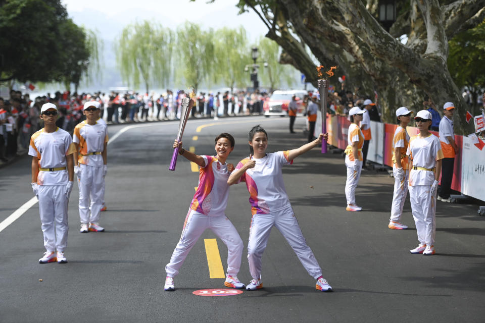 In this photo released by Xinhua News Agency, torch bearers Wang Shuang and Wang Qinou at right poses for photos during the torch relay of the 19th Asian Games in Hangzhou in eastern China's Zhejiang Province on Friday Sept. 8, 2023. The Asian Games open in two weeks, the first multi-sport international event in China since pandemic restrictions were lifted there about nine months ago,Unmatched for size, the Asian Games may even surpass the Olympics for controversy, power politics and intrigue. (Huang Zongzhi/Xinhua via AP)