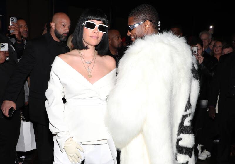 A woman with shoulder length hair, bangs wearing white sunglasses and a white outfit next to Usher in a matching outfit