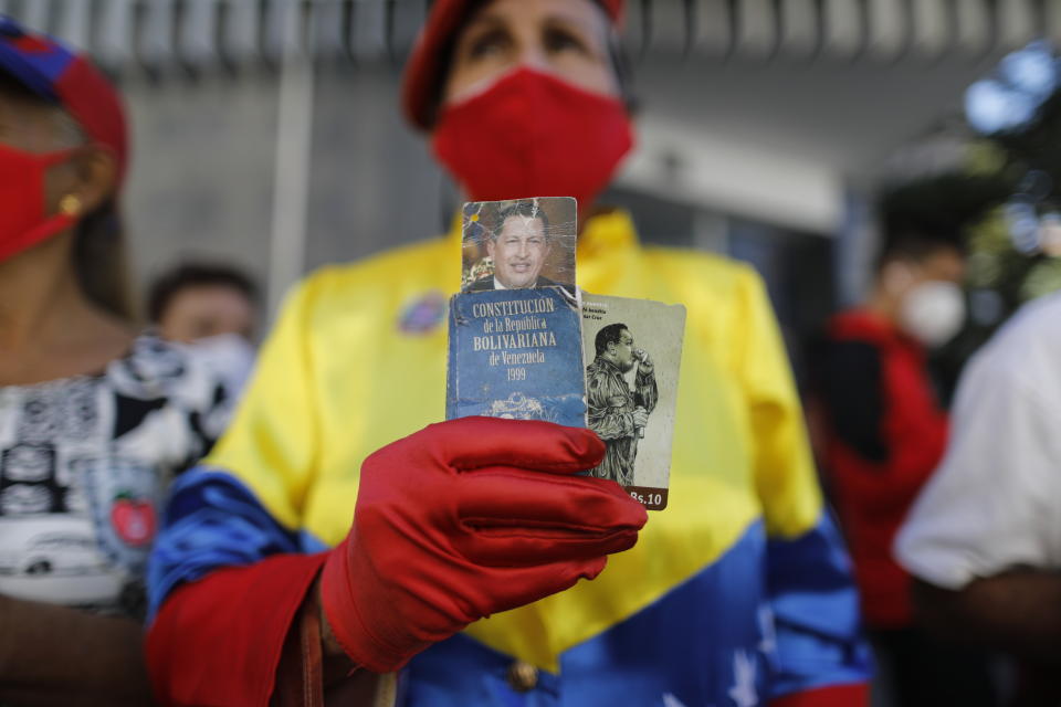 A government supporter Julia Mercedes Gutierrez holds photos of late Venezuelan President Hugo Chavez and a small version of the national constitution outside the National Assembly where lawmakers are being sworn-in, in Caracas, Venezuela, Tuesday, Jan. 5, 2021. The ruling socialist party assumed the leadership of Venezuela's congress on Tuesday, the last institution in the country it didn't already control. (AP Photo/Ariana Cubillos)