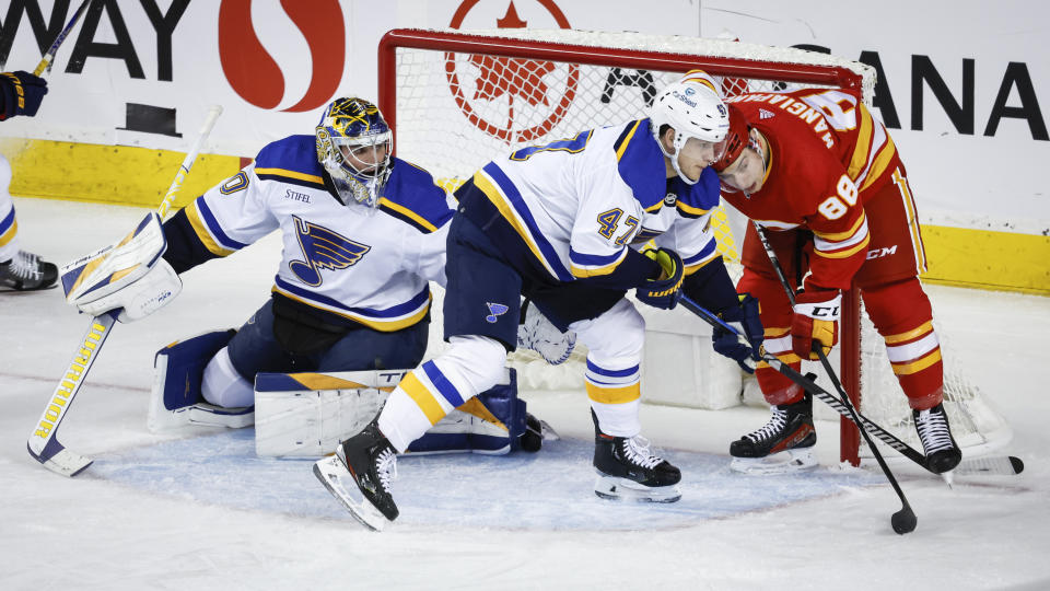 St. Louis Blues defenceman Torey Krug, center, checks Calgary Flames forward Andrew Mangiapaner, right, as goalie Joel Hofer looks on during the second period of an NHL hockey game in Calgary, Alberta, Thursday, Oct. 26, 2023. (Jeff McIntosh/The Canadian Press via AP)