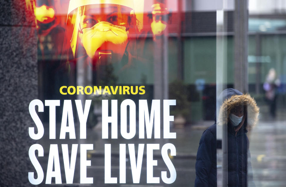 Una mujer pasa cerca de un anuncio gubernamental que pide a las personas mantenerse en casa para salvar vidas frente al coronavirus en el centro de Londres, el jueves 14 de enero de 2021, durante el tercer confinamiento nacional para frenar la propagación de la enfermedad. (Dominic Lipinski/PA vía AP)