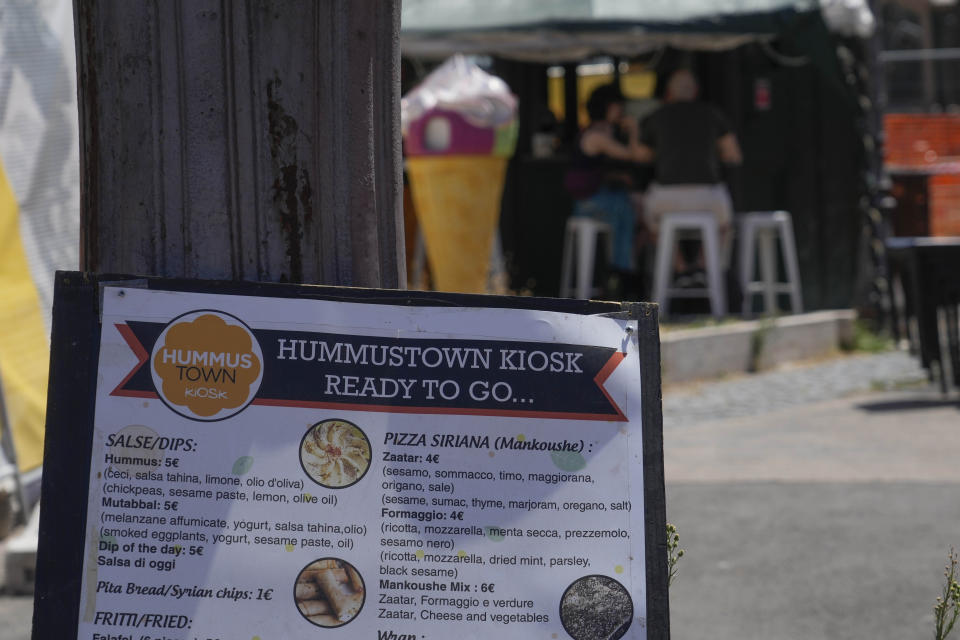 A menu is displayed outside a HummusTown kiosk in Rome, Saturday, July 27, 2024. A pair of Syrians have created community that provides support to migrants and vulnerable people in Rome, by sharing the flavors of a homeland torn by civil war. Created in 2018 as a "humanitarian catering service," HummusTown originally aimed at raising funds for families and friends in Syria. (AP Photo/Gregorio Borgia)