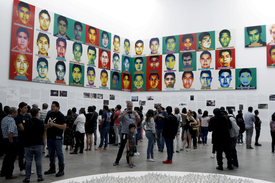 People stand under the portraits of 43 college students who went missing in 2014 in an apparent massacre, by Chinese concept artist and government critic Ai Weiwei at the Contemporary Art University Museum (MUAC ) in Mexico City, Mexico, Saturday, April 13, 2019. Each portrait in the work of art titled "Reestablish Memories" is made out of lego blocks. (AP Photo/Claudio Cruz)