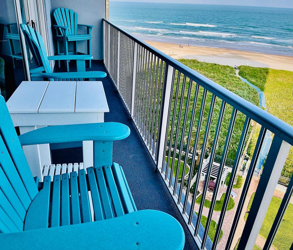 Blue chairs on a balcony overlooking a beach.
