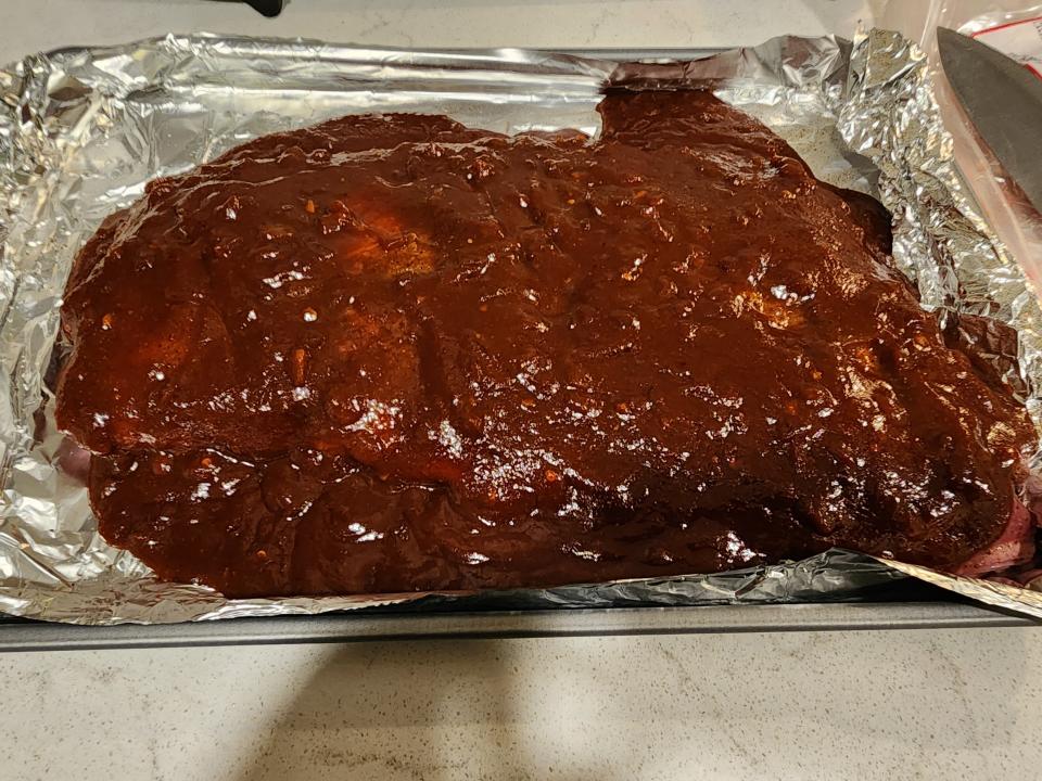ribs covered in barbecue sauce on a foil lined baking tray