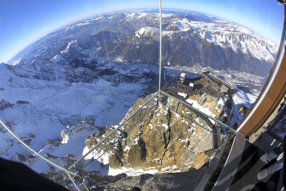 In this photo taken on Tuesday, Dec. 17, 2013, mountains are seen through a glass cage named 'Pas dans le Vide' (Step into the Void) at the top of the Aiguille du Midi peak (3842-meters high or 12,604 feet), in the French Alps, during a press visit. Visitors can enjoy the view of Mont Blanc, Europe's highest mountain, from the platform. The attraction opens Saturday. (AP Photo/Alexis Moro)