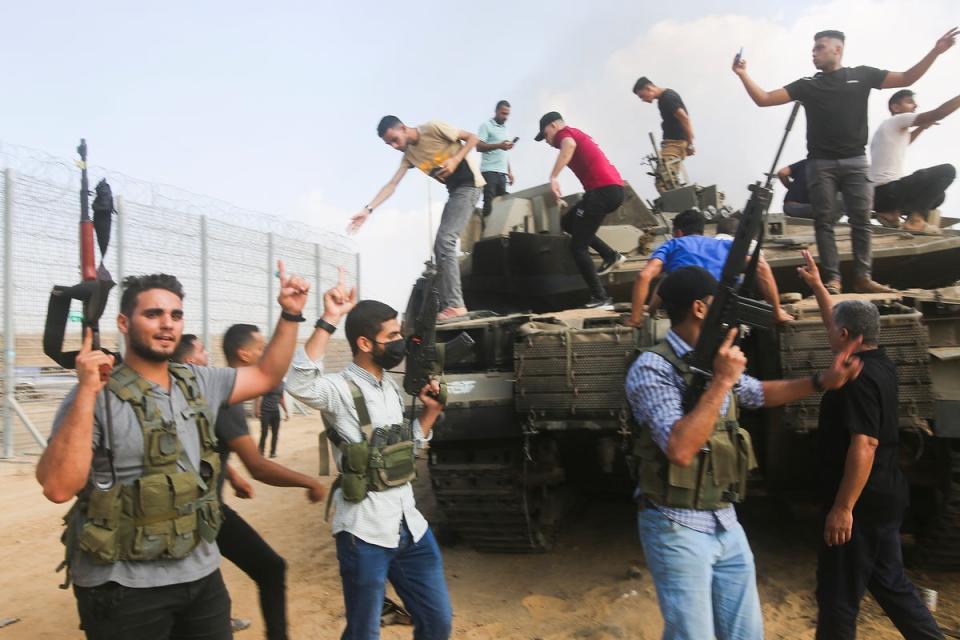 Palestinian militants celebrate by an Israeli tank at the border fence of the Gaza Strip on Saturday (AP)
