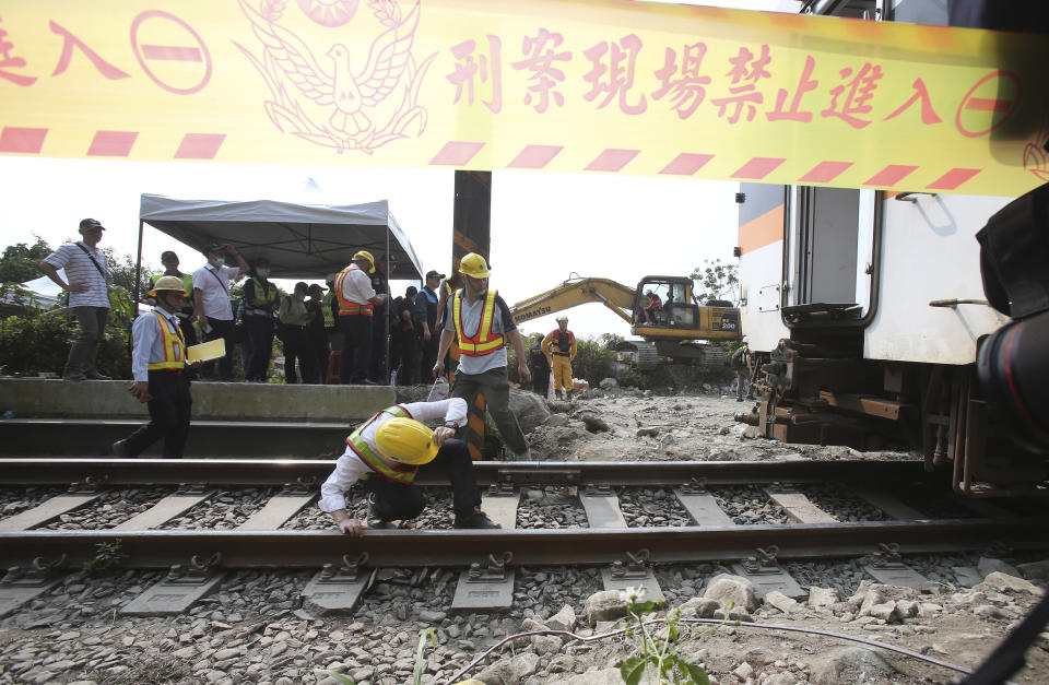 Workers inspect near the derailed train near Taroko Gorge in Hualien, Taiwan on Saturday, April 3, 2021. The train partially derailed in eastern Taiwan on Friday after colliding with an unmanned vehicle that had rolled down a hill, killing and injuring dozens. Workers began removing some of the train cars and repair work also has begun on the tracks including the tunnel where part of the eight-car train crashed. (AP Photo/Chiang Ying-ying)