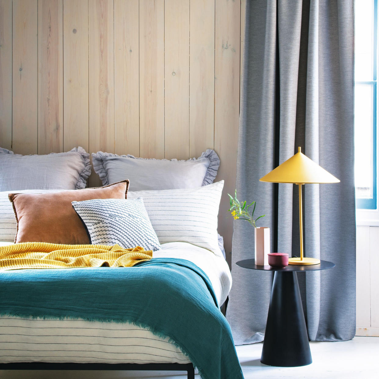  Bedroom with colourful bedding, bedside table, table lamp, and grey curtains. 