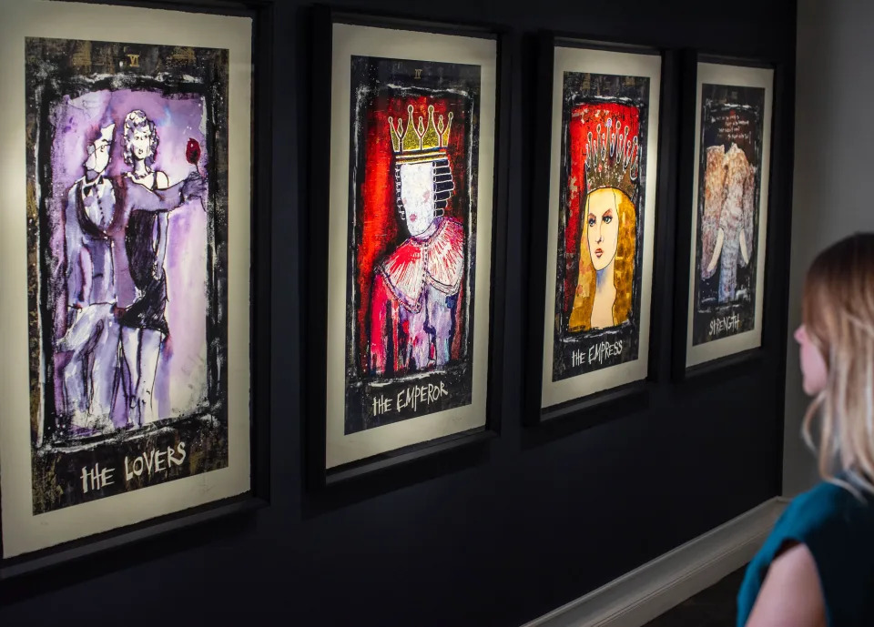 A woman looks at four paintings hanging on a dark background