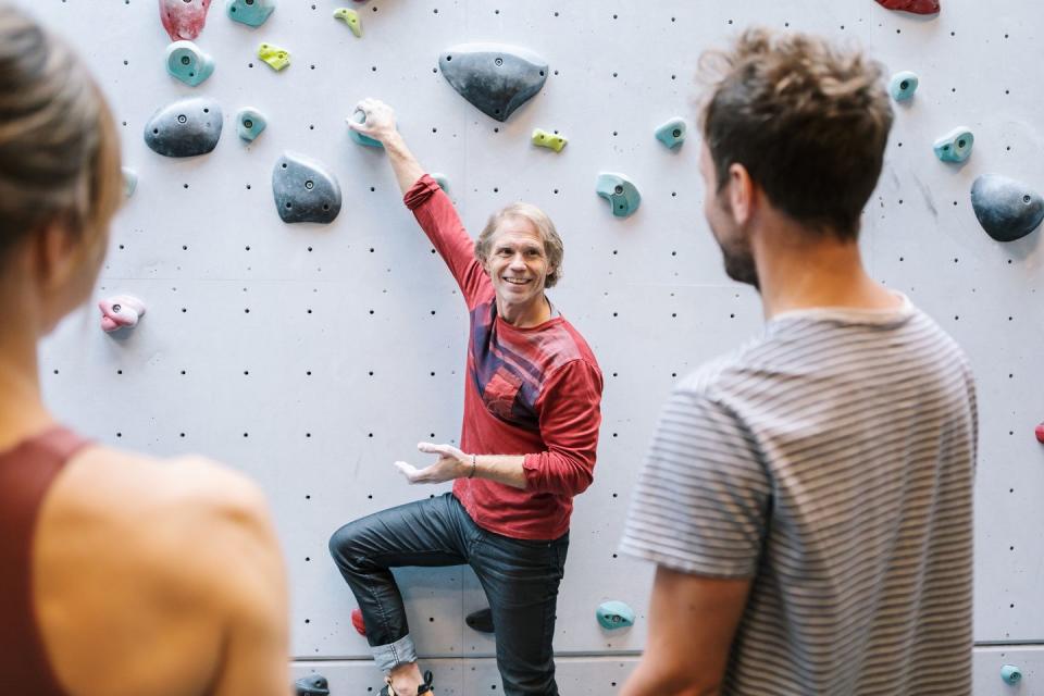 smiling mature instructor teaching male and female students about bouldering in gym