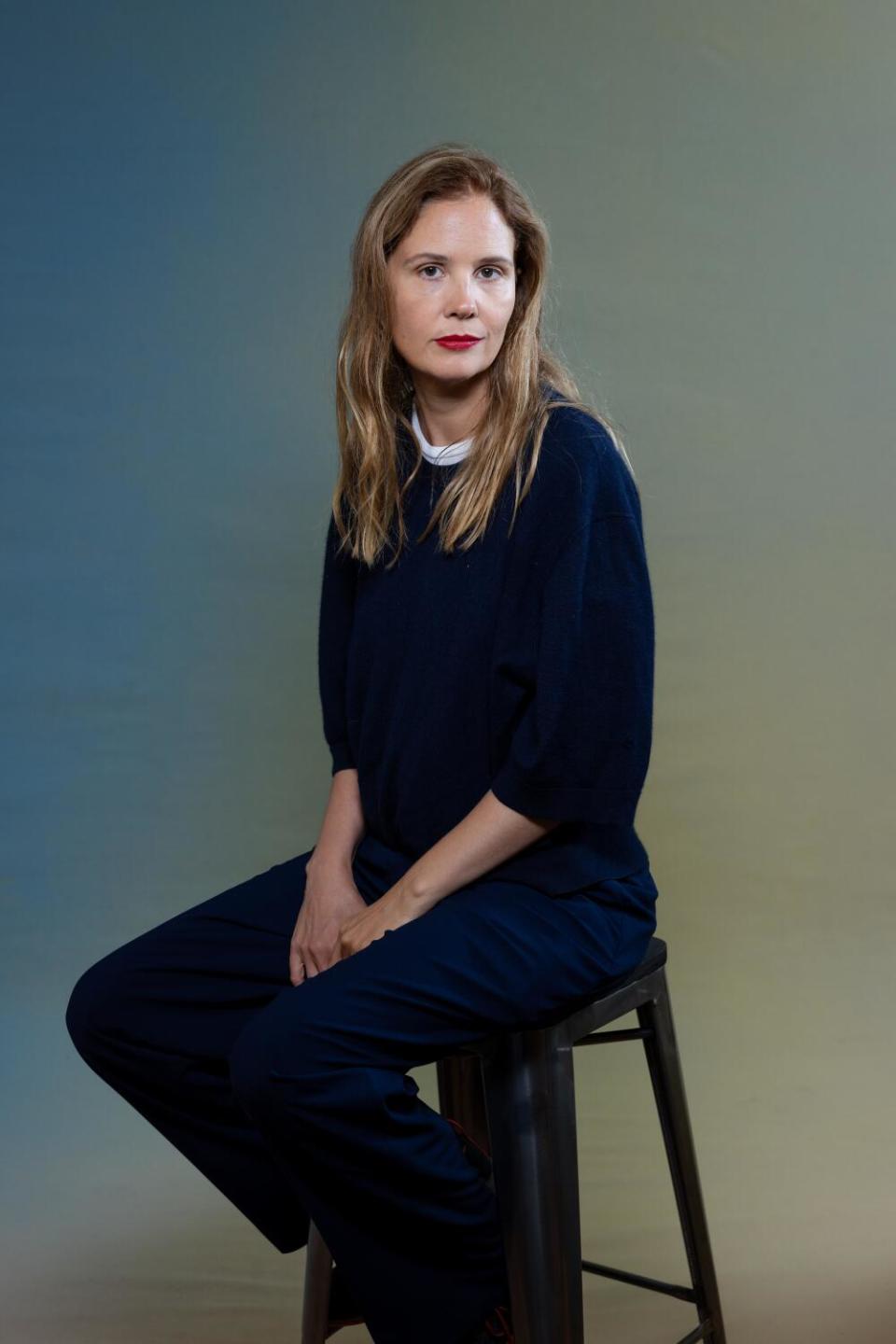 Justine Triet in a dark outfit sits on a black stool.