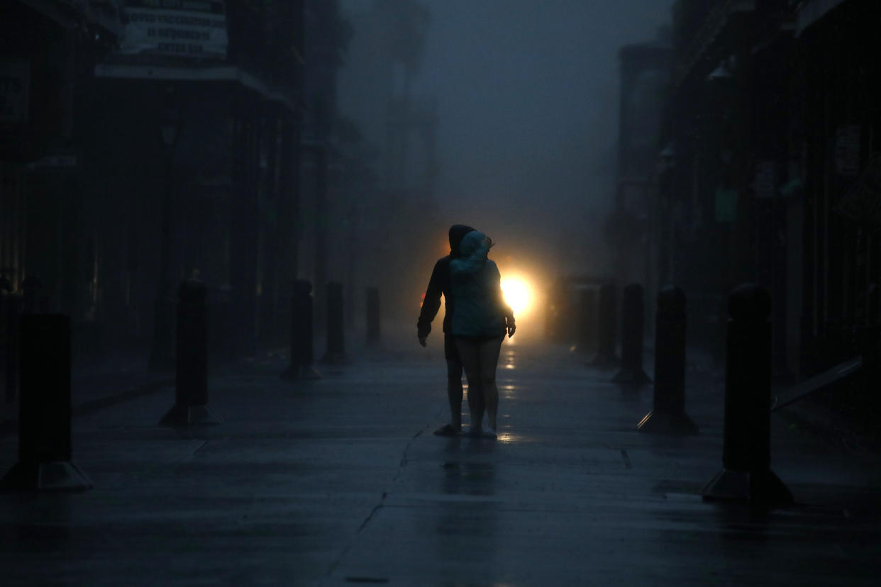 Two people stand on a path between buildings at night, illuminated by a sole light source behind them.