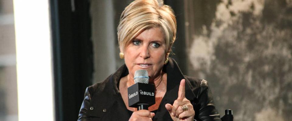 Suze Orman holds a microphone and points her finger at someone off camera