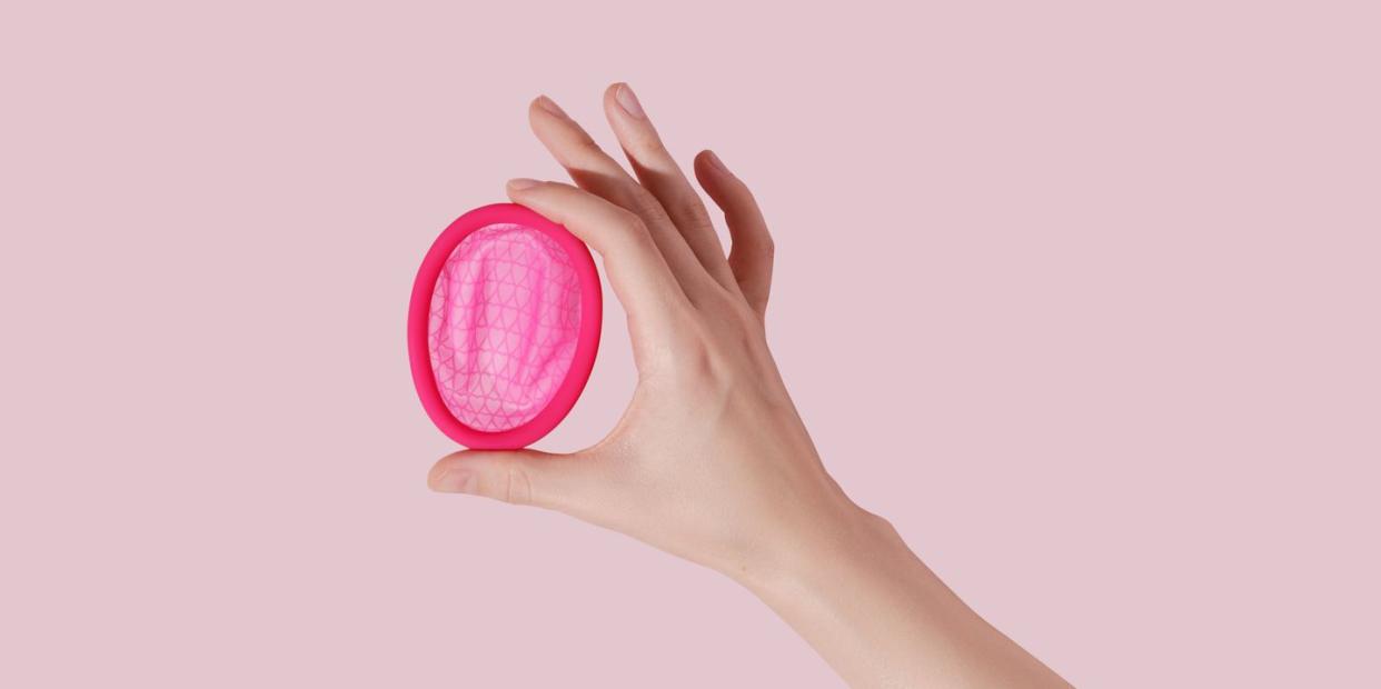 a hand holding a pink menstrual disc against a pink background