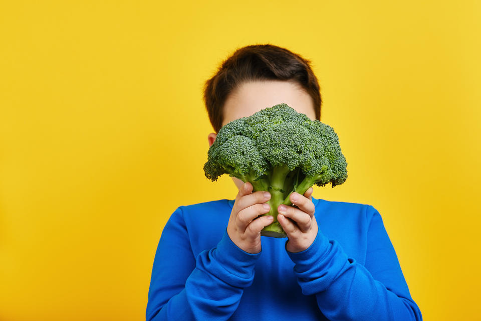 Child holding broccoli in front of face, playful concept on encouraging kids to eat vegetables