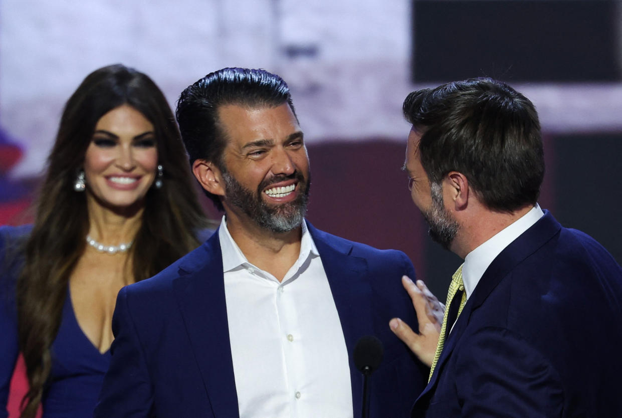 JD Vance speaks with Donald Trump Jr. onstage as Kimberly Guilfoyle looks on.