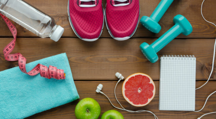 A photo of workout gear, including sneakers, water, weights and a towel, laid out on a wooden floor.
