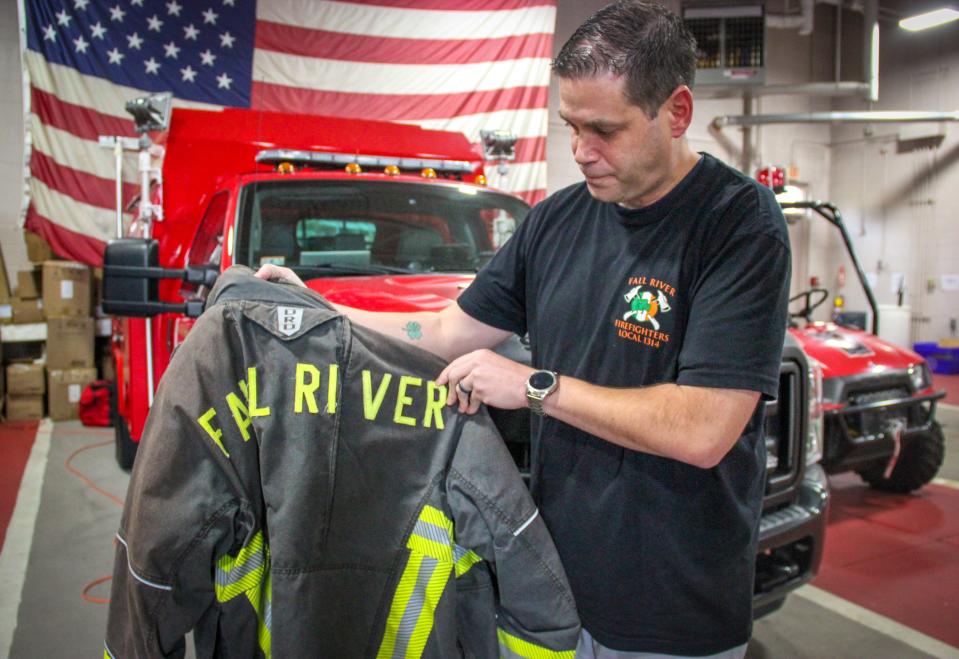 Fall River firefighter Jason Burns holds up a piece of firefighting turnout gear made with PFAS chemicals, at the North End fire station on Commerce Drive.