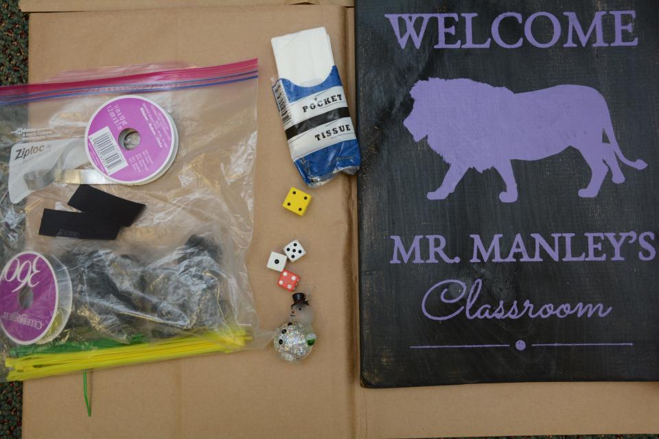 A crime scene photo taken of items found in Hector Manley's Parkside Elementary classroom. Among other things is a wooden sign painted black, with a purple lion in the middle. The text welcomes the reader to Mr. Manley's classroom.
