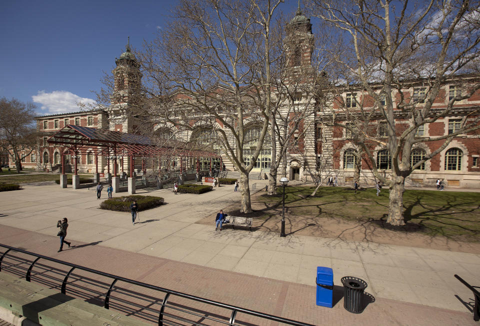 FILE - Tourists walk around the grounds at Ellis Island, on April 29, 2015, in New York. The location is featured in a collection of mini-essays by American writers published online by the Frommer's guidebook company about places they believe helped shape and define America. (AP Photo/Julie Jacobson, File)