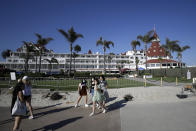 People pass the closed Hotel Del Coronado Thursday, June 11, 2020, in Coronado, Calif. California's tourism industry is gearing back up with the state giving counties the green light to allow hotels, zoos, aquariums, wine tasting rooms and museums to reopen Friday. (AP Photo/Gregory Bull)