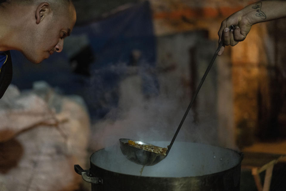 Martin Benitez, 35, left, checks the dinner that he prepared for neighbors at a soup kitchen that he organized at Puerta 8, a low income neighborhood north of Buenos Aires, Argentina, Wednesday, Feb. 9, 2022, where contaminated cocaine may have been sold. A batch of that toxic cocaine has killed at least 23 people and hospitalized many more, according to police. (AP Photo/Rodrigo Abd)