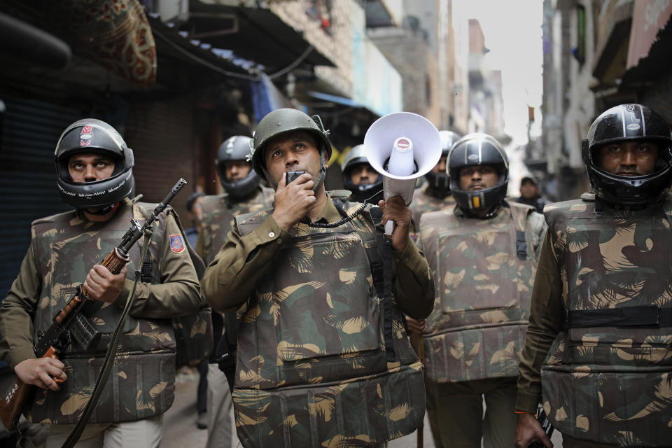 A Delhi police officer makes announcements to warn residents from venturing outside their homes as Indian security officers patrol a street in New Delhi, India, Wednesday, Feb. 26, 2020. At least 20 people were killed in three days of clashes in New Delhi, with the death toll expected to rise as hospitals were overflowed with dozens of injured people, authorities said Wednesday. The clashes between Hindu mobs and Muslims protesting a contentious new citizenship law that fast-tracks naturalization for foreign-born religious minorities of all major faiths in South Asia except Islam escalated Tuesday. (AP Photo/Altaf Qadri)