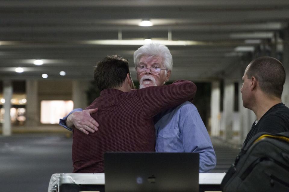 Capital Gazette reporters Pat Furgurson, center, and Chase Cook hug at a makeshift office