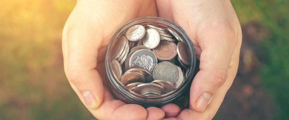 Man's hands hold a glass jar with a coins (toned, 