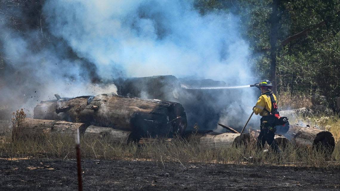 A firefighter extinguishes flames burning a stack of logs near Darrah and Triangle roads as the Oak Fire moves through the area east of Mariposa on Saturday, July 23, 2022.