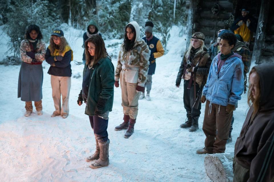 A group of girls are standing outside in the snow, bundled in coats, and they are looking in the same direction.