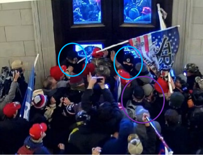 In this still image from a surveillance video shared by federal prosecutors in court filings, a group of rioters inside the U.S. Capitol on Jan. 6, 2021, pushes against two police officers, circled in blue, who were attempting to keep an exterior door shut against the mob. Iowan Daryl Johnson and his son, Daniel, circled in purple, are seen near the front of the group.