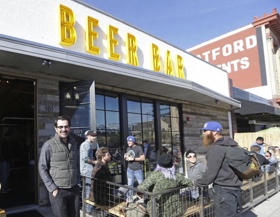 In this April 16, 2014 photo, actor Ty Burrell, who plays bumbling dad Phil Dunphy on ABC's “Modern Family,” left, poses outside Beer Bar in Salt Lake City. Burrell just opened the beer garden-like eatery that serves 150 beers paired up with an array of house-made bratwursts, local breads and Belgian fries. The restaurant, which sports long tables and benches with high ceilings to evoke that Bavarian beer hall feel, is next door to the cocktail bar Burrell co-owns with an equally simple name, Bar X. (AP Photo/Rick Bowmer)