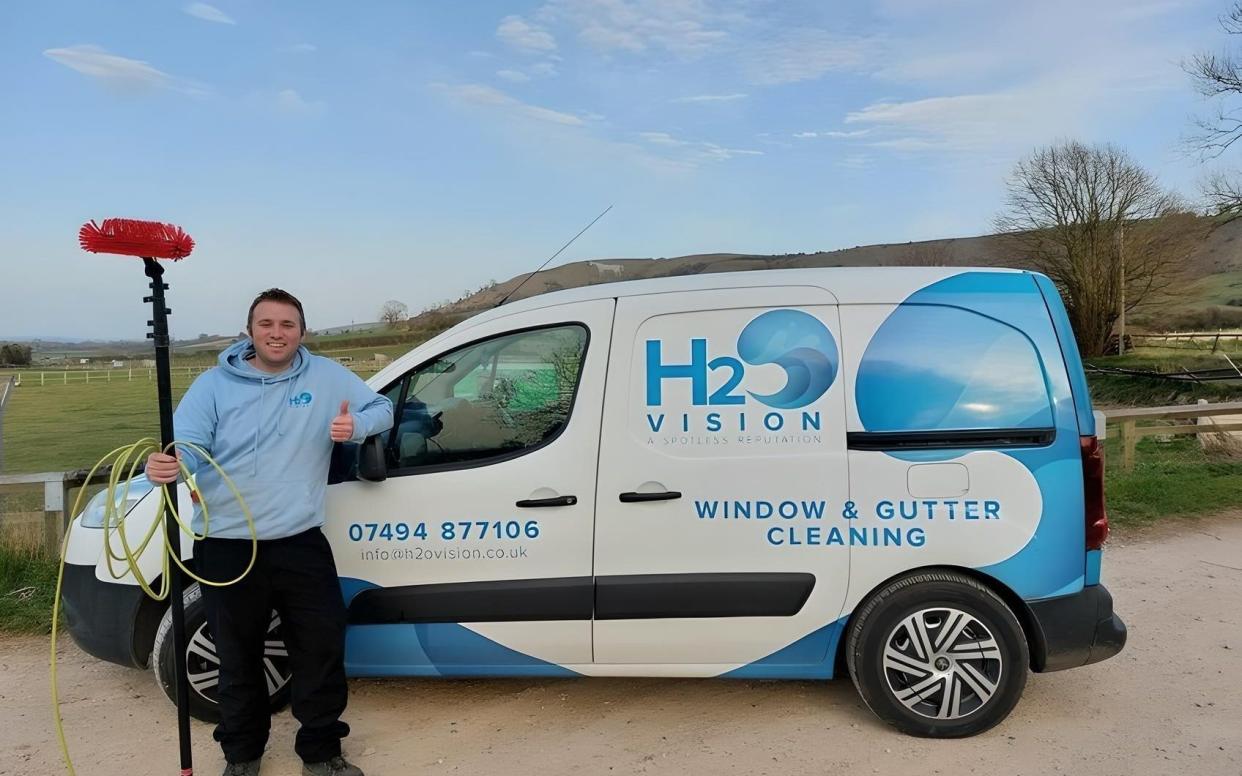 Mr Knight gives a thumbs-up sign as he poses in front of his liveried van, holding a telescopic cleaning pole