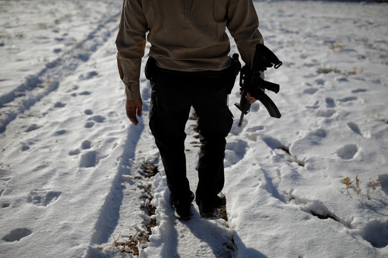 Drew Miller carries an assault rifle at a survival camp