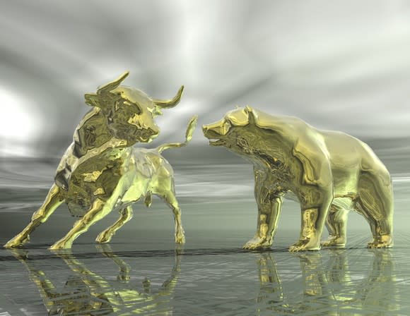 Two gold statues of a bull and a bear face off against a cloudy, grey backdrop.