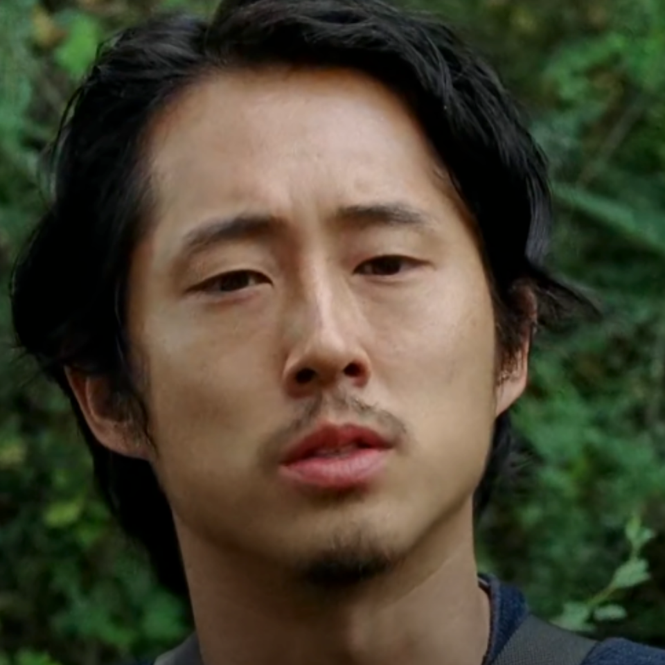 Glenn from The Walking Dead looks concerned in a forest scene
