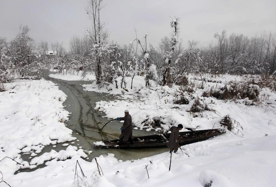 Kashmiri men try to push their boat through the waters of Anchar Lake after heavy snowfall in Srinagar