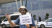 A protester holds a placard that reads: "suitcase, on the train to Moscow," as he says goodbye to expelled Russian diplomatic staff at Sofia's airport Sunday, July 3 2022. Two Russian airplanes were set to depart Bulgaria on Sunday with scores of Russian diplomatic staff and their families amid a mass expulsion that has sent tensions soaring between the historically close nations, a Russian diplomat said. (AP Photo/Valentina Petrova)