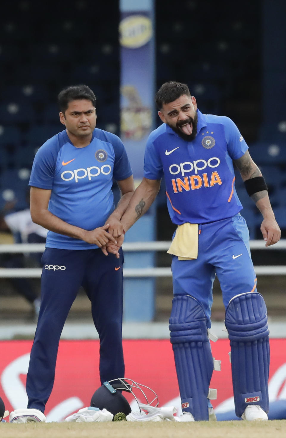 India captain Virat Kohli, right, sticks out his tongue after injuring his thumb while batting a shot off West Indies wicketkeeper Kemar Roach during their third One-Day International cricket match in Port of Spain, Trinidad, Wednesday, Aug. 14, 2019. (AP Photo/Arnulfo Franco)