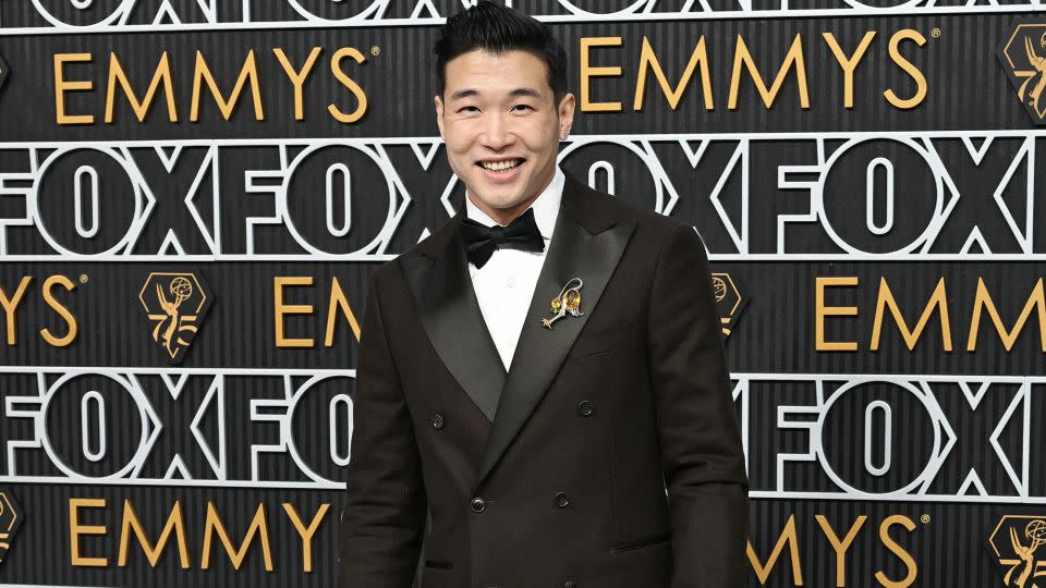 Joel Kim Booster, writer and star of "Fire Island," wore a double-breasted brown Italian wool suit by Todd Snyder with a bird brooch on his lapel. - Gilbert Flores/Variety/Getty Images