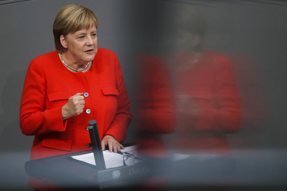 In this photo taken with a reflection in a window of the visitors tribune, German Chancellor Angela Merkel delivers her speech during a plenary session of the German parliament Bundestag about the budget 2019, in Berlin, Wednesday, Sept. 12, 2018. (AP Photo/Markus Schreiber)