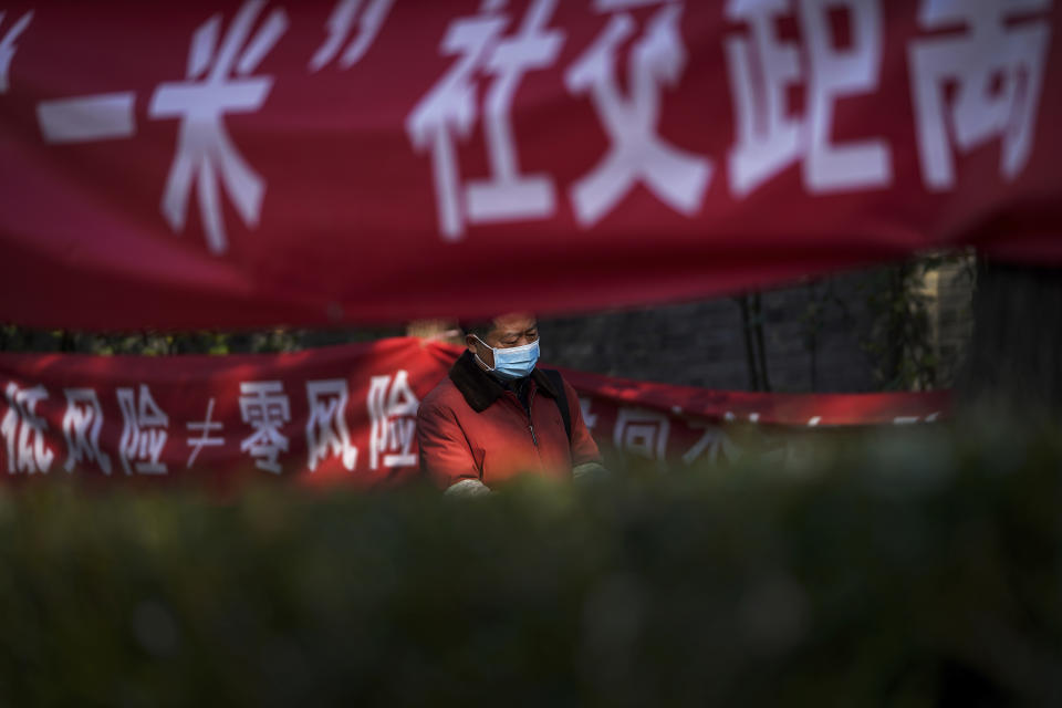 A man wearing a face mask to help curb the spread of the coronavirus walks by propaganda banners displaying coronavirus precaution messages along a neighborhood alley in Beijing, Sunday, Nov. 29, 2020. (AP Photo/Andy Wong)