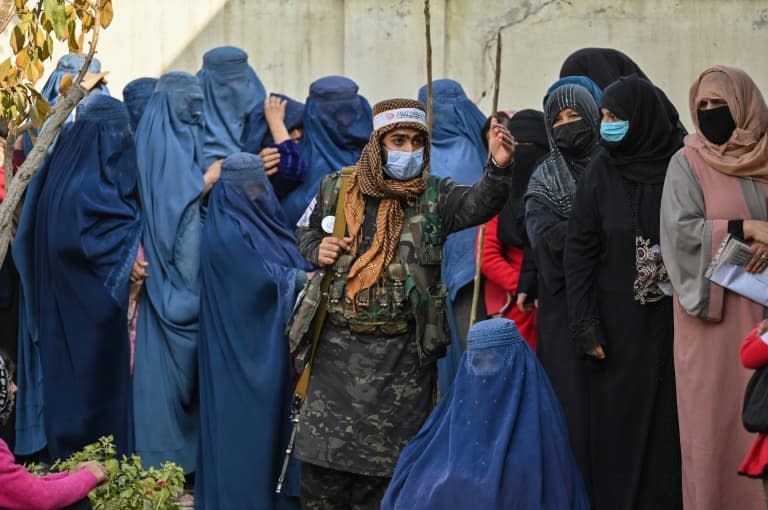 Un combattant taliban monte la garde devant des femmes qui attendent pour une distribution d'argent organisée par le Programme alimentaire mondial, à Kaboul le 29 novembre 2021 - Hector RETAMAL © 2019 AFP