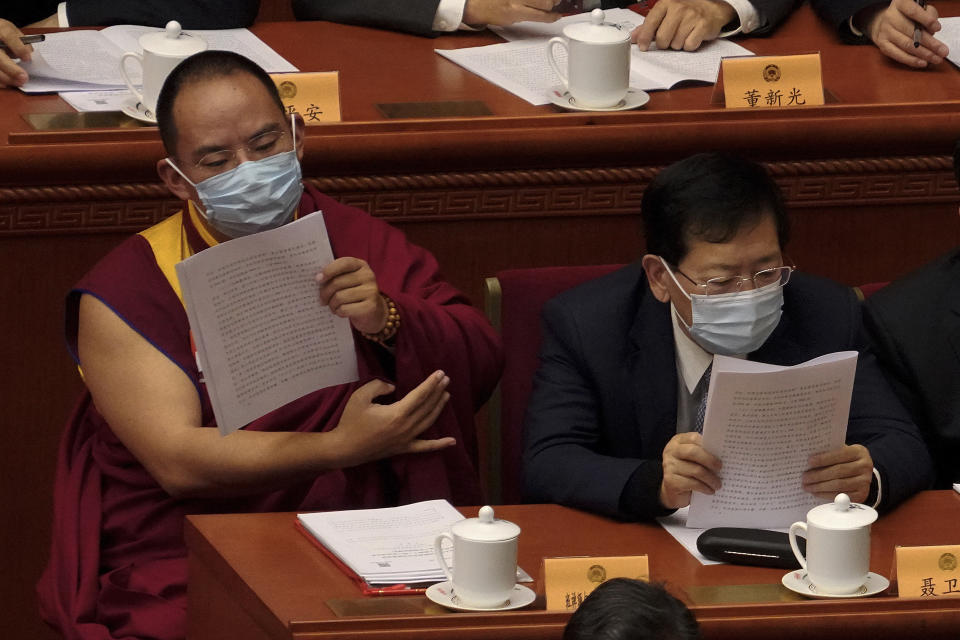 The 11th Panchen Lama Bainqen Erdini Qoigyijabu, left, a member of the National Committee of the Chinese People's Political Consultative Conference (CPPCC), left, wearing a face mask looks at a work reports during the opening session of the CPPCC at the Great Hall of the People in Beijing, Thursday, March 4, 2021. (AP Photo/Andy Wong)