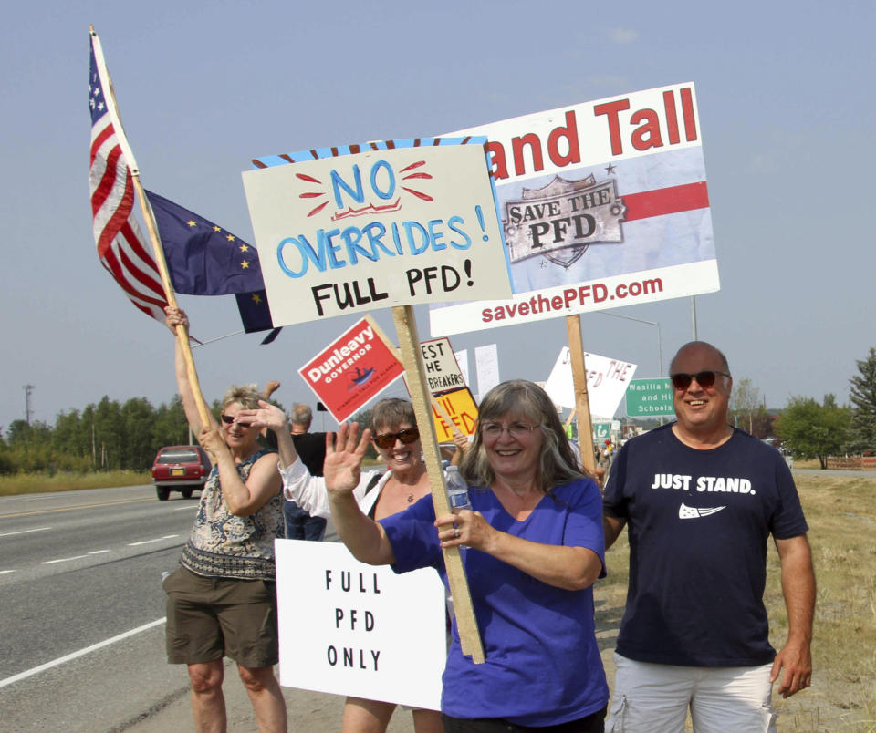 FILE - In this July 8, 2019 file photo, supporters of a fully funded oil check hold signs in Wasilla, Alaska. For decades, Alaska has had an uneasy reliance on oil, building budgets around its volatile boom-or-bust nature. When times were rough, prices always seemed to rebound, forestalling a day of reckoning some believe may finally have come. The situation has politicians weighing changes to the annual dividend paid to residents from earnings of the state's oil-wealth fund, the Alaska Permanent Fund. (AP Photo/Mark Thiessen, File)