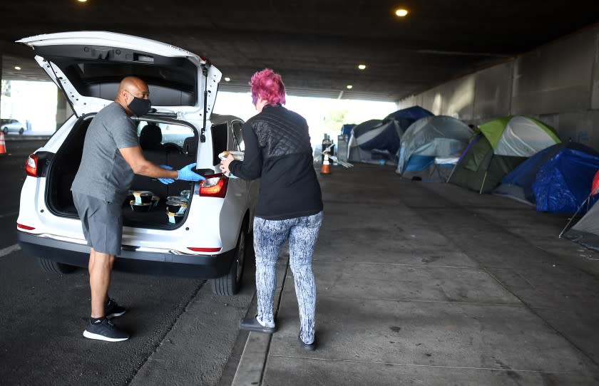 LOS ANGELES, CALIFORNIA MAY 19, 2020-Tom Crump hands out free lunch to a homeless woman on Venice Blvd. under the 405 Freeway in Los Angeles Tuesday. Thousands of homeless people living near freeways in L.A. County are in line to receive alternative shelter during the COVID-19 pandemic. (Wally Skalij/Los Angeles Times)