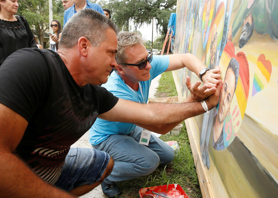 <p>Saul Barrios (L) leaves his handprint on a mural that contains an image of his deceased son Alejandro Barrios Martinez, with the help of artist Yuri Karabash, at the memorial outside the Pulse Nightclub on the one-year anniversary of the shooting in Orlando, Florida, June 12, 2017. (Scott Audette/Reuters) </p>